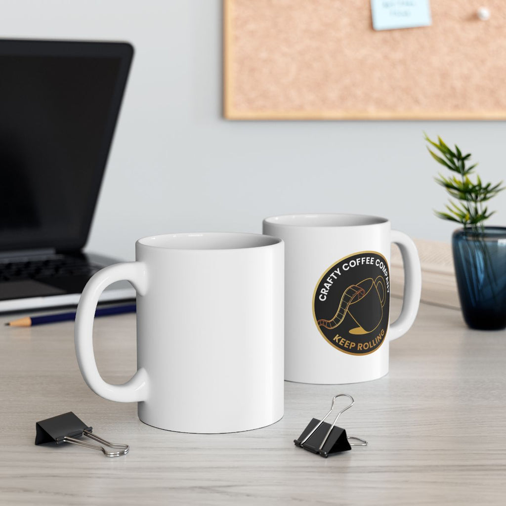 Two white mugs with a Crafty Coffee Company logo on a desk next to a laptop and decorative plant