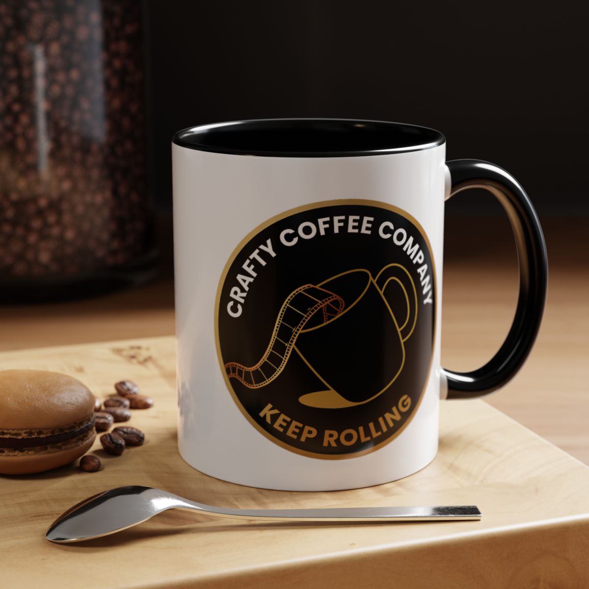 White mug with black interior and handle, featuring 'Crafty Coffee Company' logo, on a wooden surface with coffee beans and a spoon.